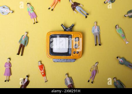 Figurine persone intorno retro syled piccolo televisore su sfondo giallo Foto Stock