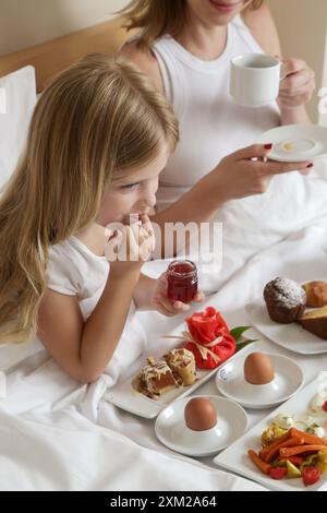 La madre e la sua bambina fanno colazione a letto in una camera d'albergo Foto Stock