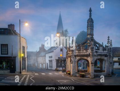 Malmesbury, Wiltshire, Inghilterra - la storica Market Cross nel centro di Malmesbury in una mattina nebbiosa a luglio, poco prima dell'alba. Foto Stock