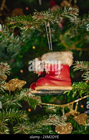 Gli stivali rossi di Babbo Natale decorati con una pelliccia bianca sono appesi a un albero di Natale verde Foto Stock