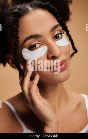 Una giovane donna afroamericana con macchie per gli occhi su sfondo beige. Foto Stock