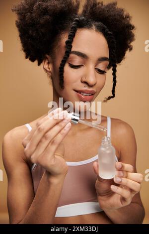 Una giovane donna afroamericana con un bel sorriso applica prodotti per la cura della pelle con un contagocce. Foto Stock