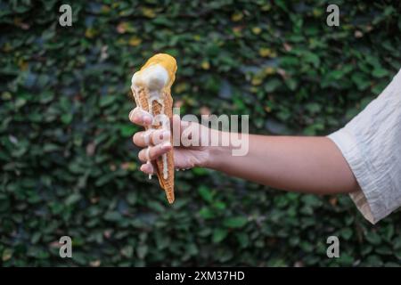 Primo piano di una donna che tiene a mano il cono di waffle con gelato alla vaniglia, che si scioglie Foto Stock