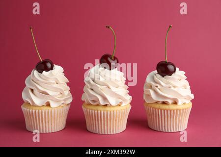 Deliziosi cupcake con panna e ciliegie su sfondo rosso Foto Stock