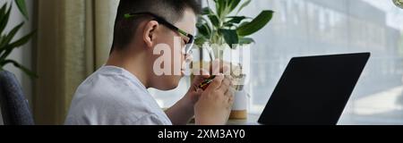 Un ragazzo con la sindrome di Down siede a una scrivania in casa sua, intensamente lavorando a un progetto artigianale. Foto Stock