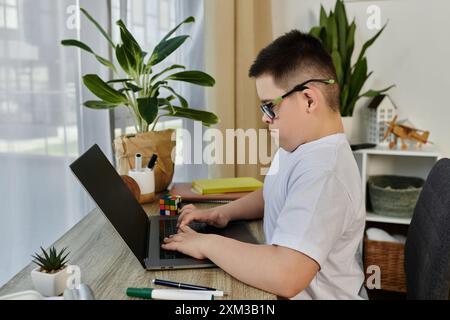 Un ragazzo con la sindrome di Down si siede alla sua scrivania, usando un portatile. Foto Stock