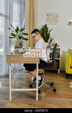 Un ragazzo con la sindrome di Down siede alla sua scrivania, concentrato sul suo lavoro. Foto Stock