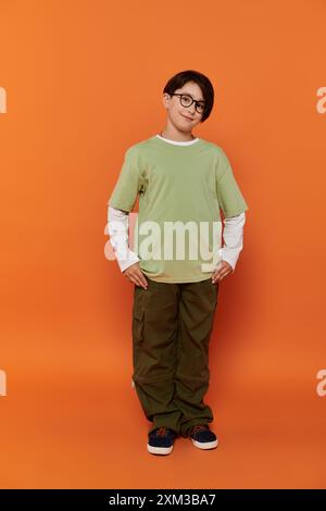 Un ragazzino sta in piedi con le mani sui fianchi, indossando una camicia verde e pantaloni kaki. Foto Stock