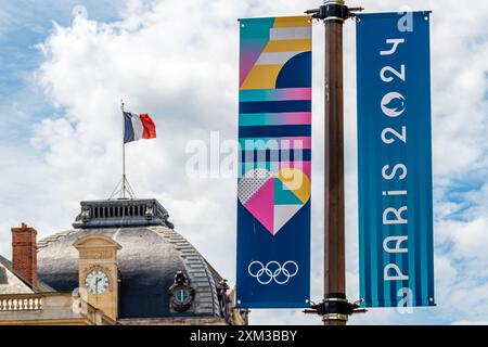 Cartelli decorativi colorati per le Olimpiadi estive di Parigi 2024 in una strada di Parigi, in Francia, con una bandiera francese che sventola su un tetto sullo sfondo Foto Stock