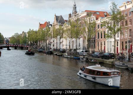 Una barca naviga lungo un canale fiancheggiato da vecchie case tradizionali di Amsterdam nel centro di Amsterdam. Foto Stock