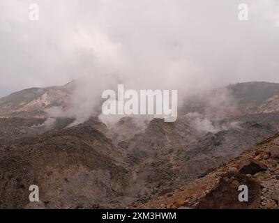 Una catena montuosa con una grande nuvola di fumo che sale dalla cima. Il fumo sta fluttuando e il cielo è nuvoloso Foto Stock