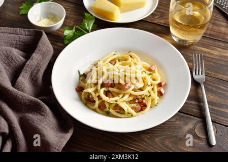 Pasta alla Carbonara, spaghetti con pancetta croccante e pepe nero su piatto bianco su tavola di legno. Cucina tradizionale italiana. Vista ravvicinata Foto Stock
