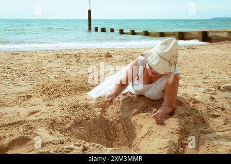 Donna matura che scavava nella sabbia su una spiaggia con un vanga di giocattoli, mai troppo vecchia. Foto Stock