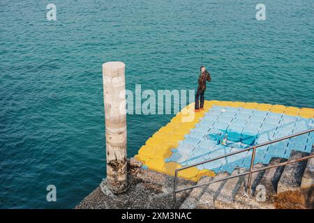 Giovane pescatore in piedi e pescare con la canna da pesca sul pontile galleggiante sul mare tropicale Foto Stock