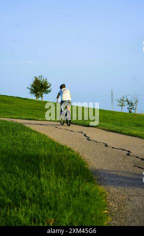 Vista posteriore dello sportivo in sella al casco protettivo, che cavalca in bicicletta sulle colline al tramonto. Immagine della motivazione sportiva. Foto Stock