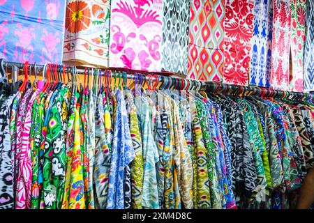 Dettaglio, vista ravvicinata di molte camicie e tessuti colorati a motivi ikat. Nella zona dei tessuti locali, la sezione di abbigliamento del famoso mercato dello shopping di Chorsu Foto Stock