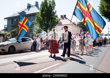 MARIEHAMN, Åland, FINLANDIA - LUGLIO 25 2024: I dignitari locali in abito tradizionale di Åland conducono migliaia di marinai per le strade durante la parata degli equipaggi delle navi del 57. Secondo giorno della terza tappa Åland della corsa delle navi alte 2024 nel porto principale, Mariehamn, Åland, Finlandia. Foto: Rob Watkins/Alamy Live News. INFO: La Tall Ships Race è un evento velico annuale che comprende navi d'alto livello storiche e moderne. Promuove l'amicizia internazionale e la formazione dei giovani, attirando partecipanti e spettatori in tutto il mondo per celebrare il patrimonio marittimo e l'arte della vela tradizionale. Foto Stock