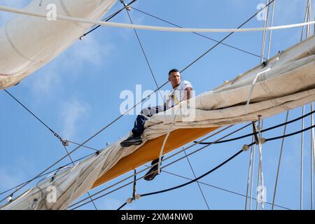 MARIEHAMN, Åland, FINLANDIA - LUGLIO 25 2024: I marinai salgono in alto nel cielo per lavorare sulle vele sugli alberi del sommergibile Guayas dall'Ecuador. Secondo giorno della terza tappa Åland della corsa delle navi alte 2024 nel porto principale, Mariehamn, Åland, Finlandia. Foto: Rob Watkins/Alamy Live News. INFO: La Tall Ships Race è un evento velico annuale che comprende navi d'alto livello storiche e moderne. Promuove l'amicizia internazionale e la formazione dei giovani, attirando partecipanti e spettatori in tutto il mondo per celebrare il patrimonio marittimo e l'arte della vela tradizionale. Foto Stock