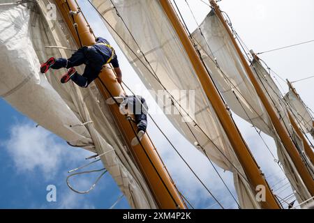 MARIEHAMN, Åland, FINLANDIA - LUGLIO 25 2024: I marinai salgono in alto nel cielo per lavorare sulle vele sugli alberi del sommergibile Guayas dall'Ecuador. Secondo giorno della terza tappa Åland della corsa delle navi alte 2024 nel porto principale, Mariehamn, Åland, Finlandia. Foto: Rob Watkins/Alamy Live News. INFO: La Tall Ships Race è un evento velico annuale che comprende navi d'alto livello storiche e moderne. Promuove l'amicizia internazionale e la formazione dei giovani, attirando partecipanti e spettatori in tutto il mondo per celebrare il patrimonio marittimo e l'arte della vela tradizionale. Foto Stock