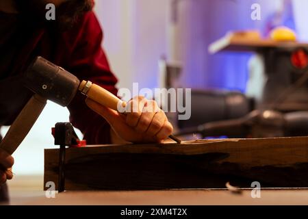 Scultore che modella il legno grezzo con scalpello e martello, crea arte del legno e taglia con precisione. Artista che realizza sculture in legno fatte a mano, incide legname con attrezzi, foto ravvicinata Foto Stock