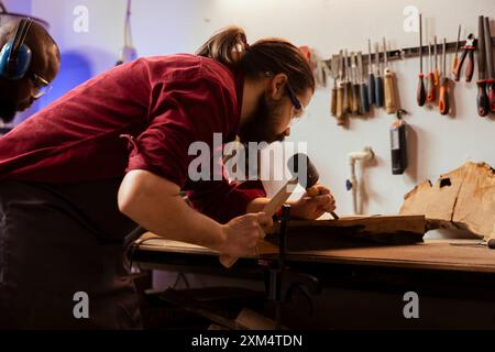 Artigiano del legno esperto nella lavorazione del legno grezzo con scalpello e martello in falegnameria, indossando occhiali di sicurezza. Esperto nella lavorazione del legno che modellava oggetti in legno, realizzava sculture in legno con dispositivi di protezione Foto Stock