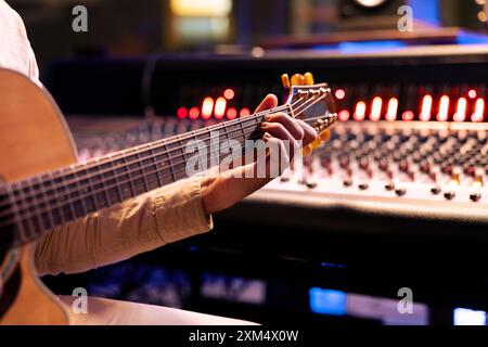 Giovane musicista che compone un nuovo brano con chitarra elettro-acustica in uno studio di musica professionale, suona strumenti e crea dischi in sala di controllo. Lavorare con Sound Designer. Primo piano. Foto Stock