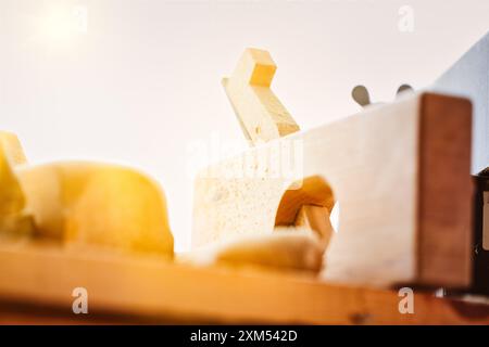 L'aereo per i falegnami è seduto su un banco da lavoro, inondato dalla luce calda del sole che scorre attraverso la vetrina del negozio. Vari altri strumenti sono sparsi in giro Foto Stock