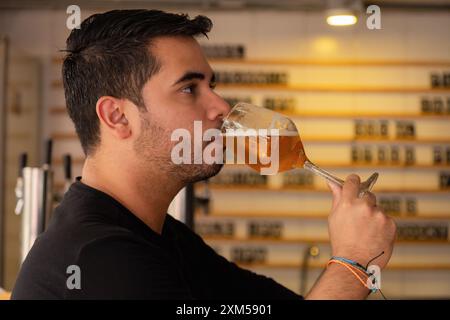 Un giovane che sorseggia un bicchiere di birra in un accogliente pub o ristorante. Foto Stock