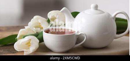 Teiera, tazza di bevanda calda e tulipani bianchi sul tavolo, primo piano Foto Stock