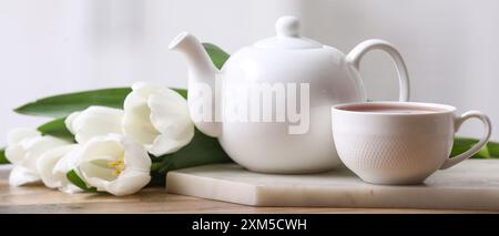 Teiera, tazza di bevanda calda e tulipani sul tavolo Foto Stock