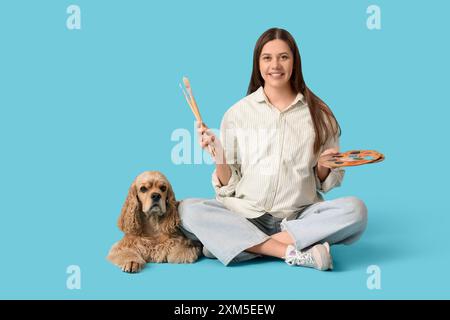 Giovane artista donna incinta con il suo cane e provviste di pittura su sfondo blu Foto Stock