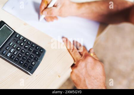 Carpenter calcola i costi e prende appunti in un'officina, concentrandosi sulla precisione e la precisione di un progetto di lavorazione del legno. La segatura riempie l'aria, Highlig Foto Stock