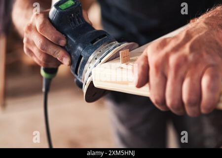 Levigatura professionale del legno in officina con precisione e precisione, utilizzando una levigatrice orbitale. La segatura riempie l'aria come si rivela la venatura del legno, mostrando oggetti di artigianato Foto Stock