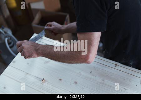 Carpenter sta levigando una tavola di legno con una pialla manuale nella sua officina, applicando antiche tecniche alla moderna lavorazione del legno Foto Stock