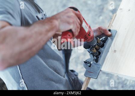 Carpenter utilizza una dima per fori da tasca e un trapano a batteria per unire due pezzi di legno. Sta lavorando a un progetto di costruzione Foto Stock