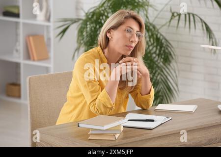 Ritratto di una bella donna matura con taccuini e libri seduti a casa Foto Stock