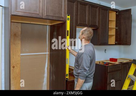 L'installazione di nuovi armadietti da cucina richiede che il lavoratore sia in piano per garantire che gli armadi siano in piano Foto Stock