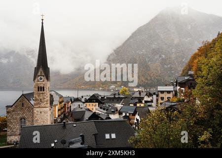 Hallstatt, Austria - 31 ottobre 2023 : pittoresco villaggio incastonato nelle Alpi austriache, con una torreggiante guglia della chiesa e nebbia che si avvolgono sulla bocca Foto Stock
