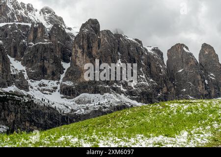 Tra la neve che si scioglie a giugno, la Sellagruppe Corvara si erge maestosamente sullo sfondo, mentre la vibrante erba verde mette in risalto il contrasto dei primi anni Foto Stock