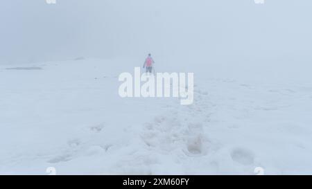 Nel cuore del paesaggio innevato della Val Vallunga, una donna forgia il suo percorso attraverso la nebbia, circondato dalle maestose Dolomiti che aggiungono un tocco di tou Foto Stock