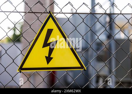 Primo piano di Un segnale di attenzione giallo ad alta tensione appeso sulla recinzione a catena. Profondità di campo bassa Foto Stock