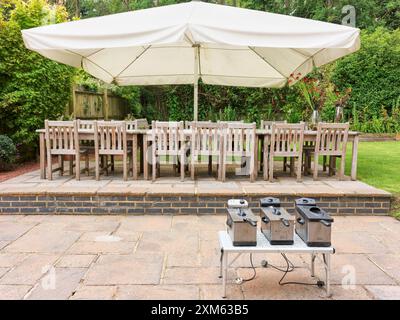 Patio (con ombrellone, tavoli e sedie e friggitrici) in un giardino inglese sul retro in una soleggiata giornata estiva. Foto Stock