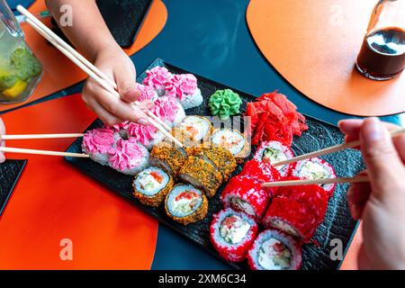 Ristorante giapponese, sushi roll di vario tipo. Le mani con le bacchette cinesi si avvicinano o portano il sushi. Foto di alta qualità Foto Stock