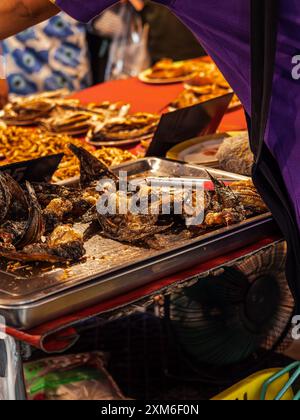 Un venditore vende pesce fritto in un mercato di Street food Foto Stock