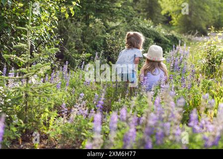 Le sorelline guardano curiosamente le api che raccolgono polline sui fiori. Foto Stock