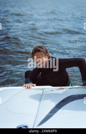 Una donna in muta sale sulla barca dopo il kitesurf. Foto Stock