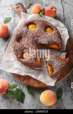 Torta al cacao al cioccolato con pesche fresche primo piano su tavola di legno. Vista dall'alto verticale Foto Stock