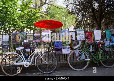 Due vecchie biciclette chiuse alle ringhiere con poster per gli eventi a Cambridge, in Inghilterra, in una giornata di sole Foto Stock