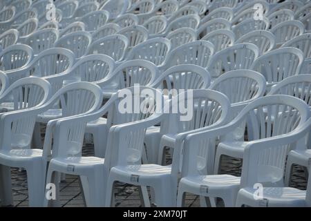 Allestimenti all'aperto con una fila di sedie di plastica bianche disposte in modo ordinato, perfette per eventi, riunioni o sedute informali nei giardini e nei patio. Foto Stock