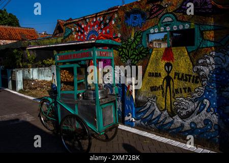 26 luglio 2024, Yogyakarta, regione speciale di Yogyakarta, Indonesia: Un venditore ambulante cammina davanti a un murale con un UFO e un murale a tema alieno nel villaggio UFO nel distretto di Mantrijeron, città di Yogyakarta. I residenti hanno collaborato per decorare il villaggio con un tema UFO e alieno per accogliere il giorno dell'indipendenza della Repubblica di Indonesia il 17 agosto. Inoltre, il villaggio UFO è inteso come una lingua per studiare l'universo, in modo che le persone siano sempre consapevoli di mantenere la pulizia nei loro rispettivi ambienti. (Immagine di credito: © Angga Budhiyanto/ZUMA Press Wire/Alamy Live News) EDITORI Foto Stock